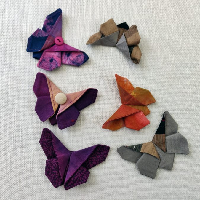 Origamiperhoset työn tekijä: Tea Savola Tekniikka ja materiaalit: taittelu pellavakankaalle, helmikoriste.