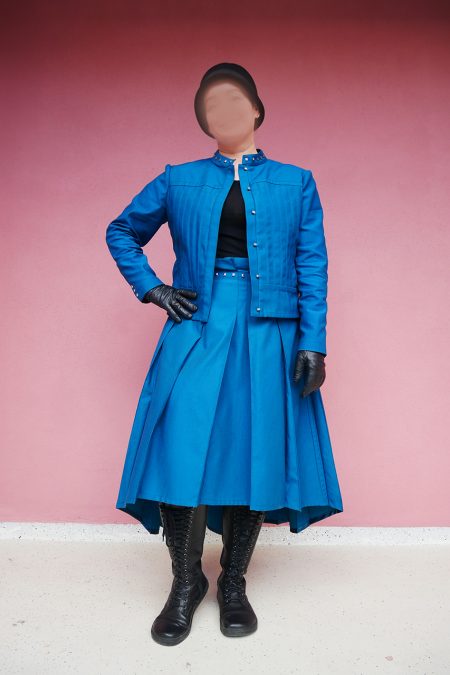 Kuva edestä, petroolinsininen jakku, näyttävä vartalonmyötäinen laskostus sekä laskoshame.