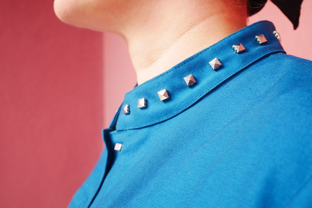 Lähikuva petroolinsinisen jakun kauluksesta, koristeena niittejä.