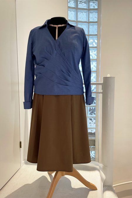 Kuva edestä, sininen pitkähihainen kietaisupaita, edessä kauniit laskokset, sekä ruskea hame.