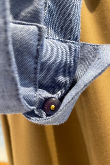 Lähikuva sinisen kietaisupaidan hihansuusta, taitetussa rannekkeessa nappikiinnitys.