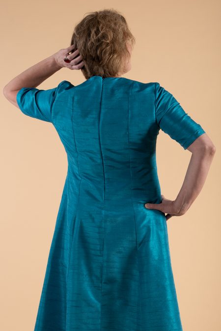 Kuva takaa, säihkyvän sininen juhlamekko, lyhyet hihat ja istuvat leikkaukset.