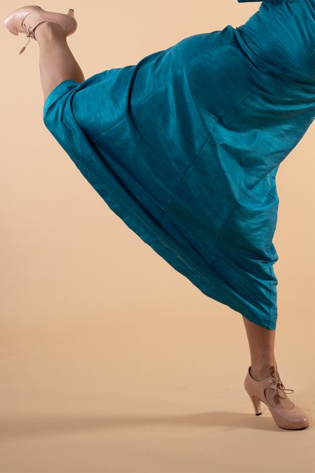 Lähikuva säihkyvänsinisen juhlamekon helmasta, yhdellä jalalla, toinen jalka kurottaa taakse.