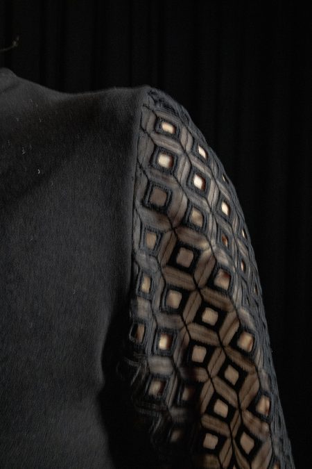 Lähikuva edestä, mustan haalarin kädentien istuva linja ja kaunis pitsihiha.