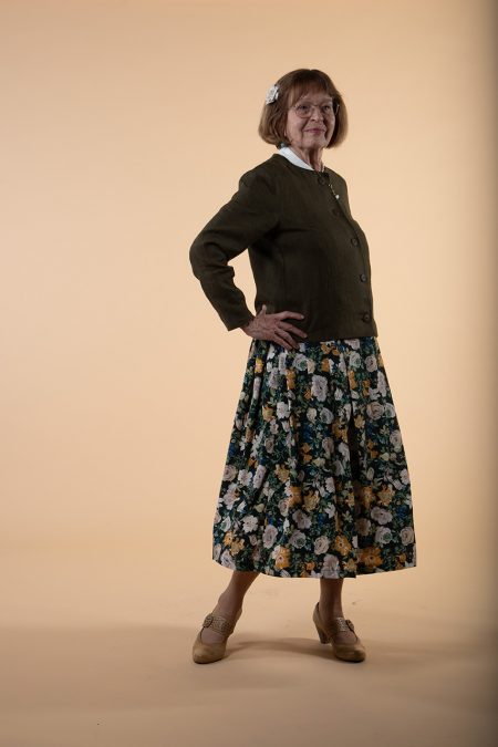 Kuva edestä, käsi lanteella, yläosa vihreää pellavaa ja hameessa kukkakuosi tummalla pohjalla.