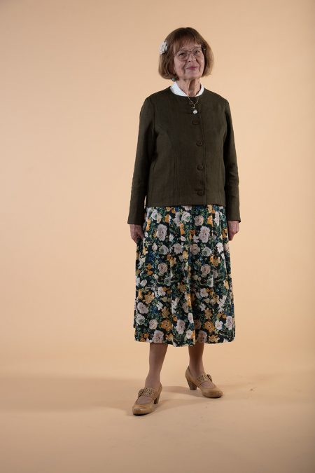 Kuva edestä, yhdistelmäasussa vihreä pitkähihainen yläosa ja kukallinen, laskostettu hame.