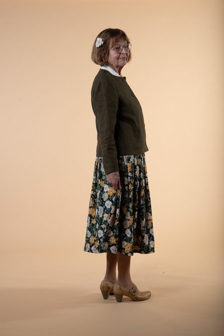 Kuva sivulta, yhdistelmäasussa vihreä pitkähihainen yläosa ja kukallinen, laskostettu hame.