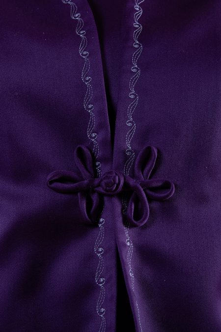 Lähikuvassa violetin villasatiinijakun kankaasta valmistettu "chinese ball button" ja lenkkikiinnitys.