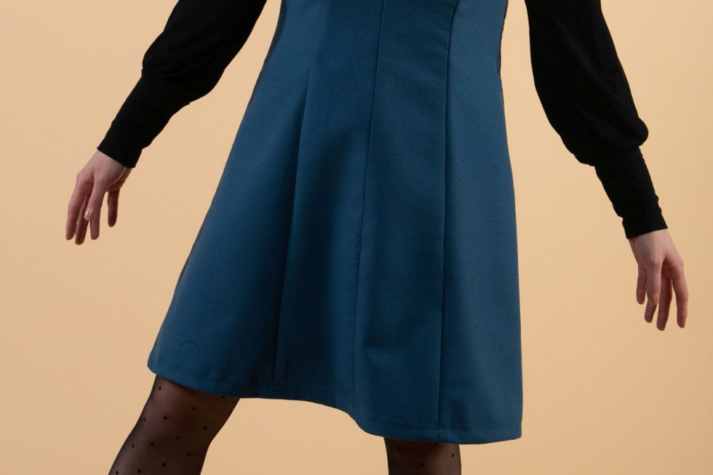 Lähikuvassa sinisen liivimekon helma, kauniit pystyleikkaukset.