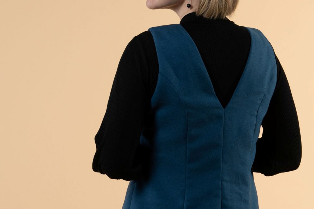 Lähikuvassa sinisen liivimekon selkä, avara v-mallinen pääntie ja prinsessaleikkaus.