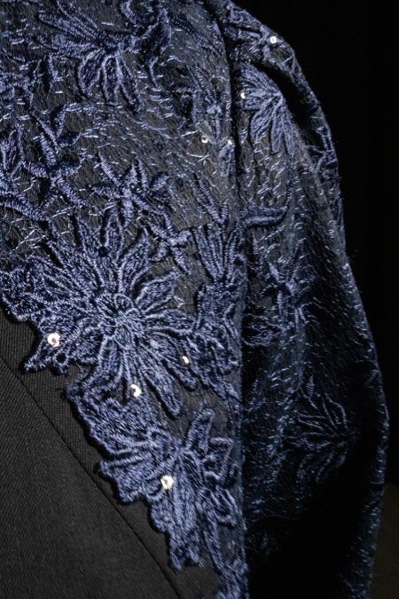 Lähikuvassa juhlamekon miehustaa ja hihaa, sininen pitsi ommeltu taidokkaasti villakankaan päälle.