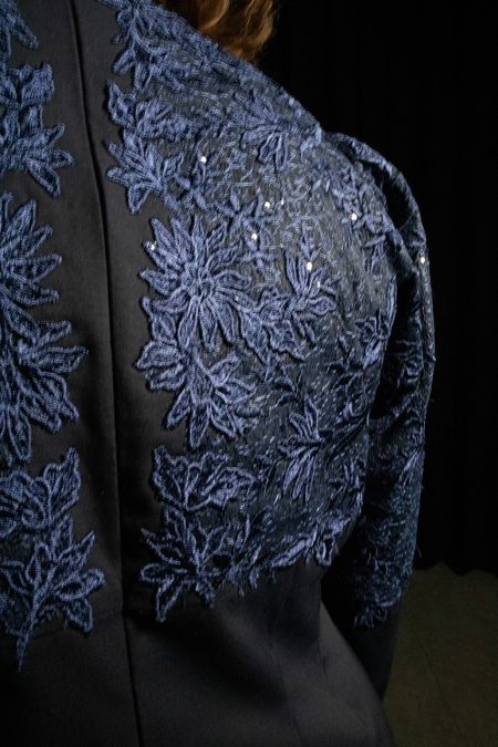 Lähikuvassa juhlamekon selkää, yläosassa villakankaan päällä sininen pitsi, keskellä piilovetoketju.