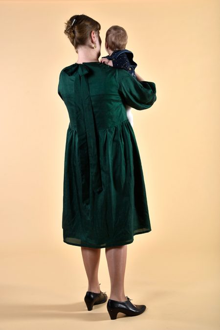 Kuva takaa, lapsi sylissä, tummanvihreä silkkimekko pitkin raglanhihoin, polvipituinen.