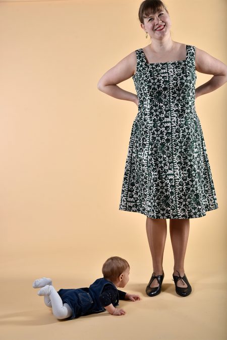 Kuva edestä, lapsi lattialla, valkovihreä hihaton polvipituinen mekko, neliömäinen pääntie.