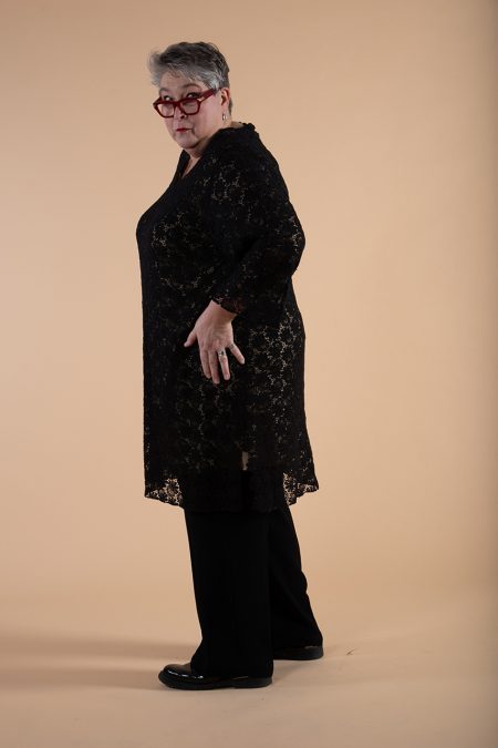 Kuva sivulta, mustan pitsitunikan suora profiili, käsi lanteella.