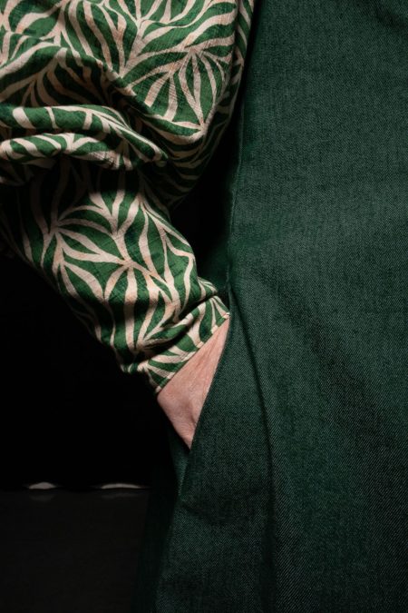 Lähikuvassa tasku vihreän liivimekon sivusaumalla, käsi taskussa, hihan korkea ranneke.