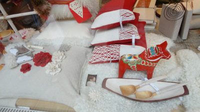 Morasta kuvattu käsityöliikkeen ikkunaa, jossa tyynyjä fransu solmuin koristeltu, puuesineitä, Taalainmaan hevonen