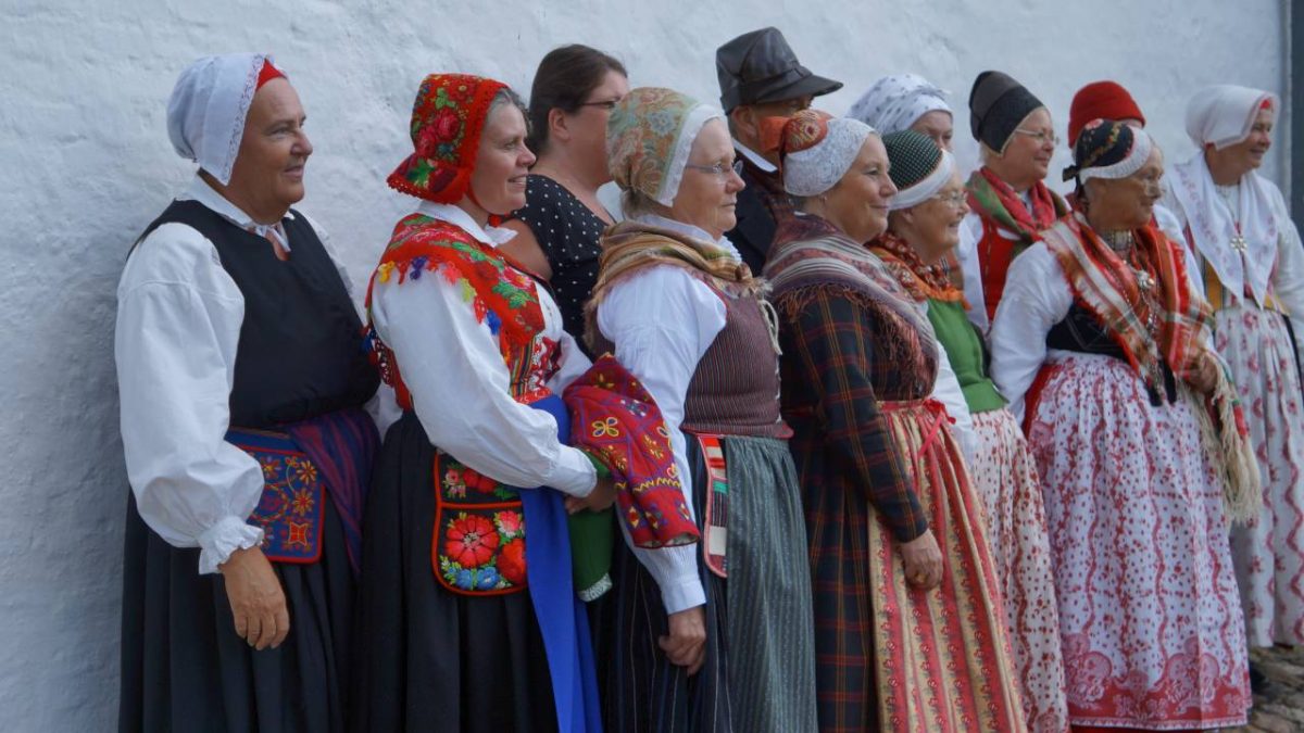 Ruotsalaisia kansallispukuja ryhmäkuvassa. Puvut ovat värikkäitä ja kuvaavat alueiden luonnetta.