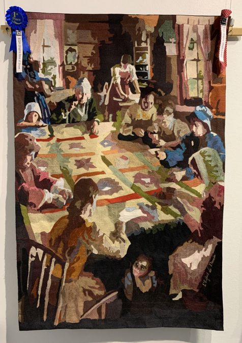 Oulun tilkkupäiviltä Eurooppaa kiertävä haastenäyttely Alkuperä-Orgins voittajatyö, jossa naiset tikkaavat pöydän ympärillä tilkkupeittoa