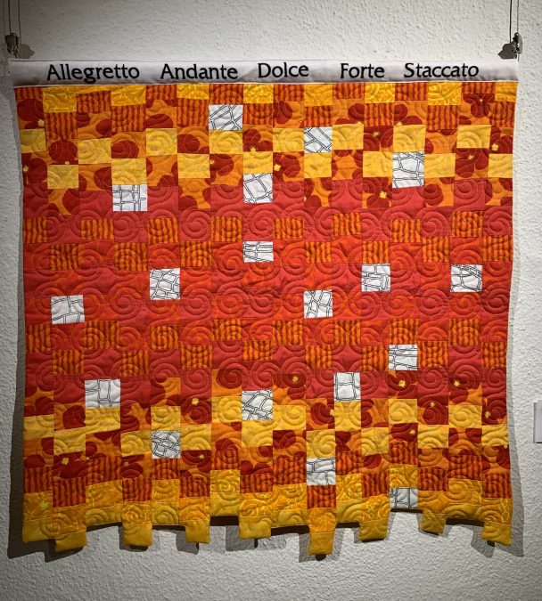 Suorakaiteen muotoinen tilkkutyö, neliöistä, jotka ovat punaisia oranssin keltaisia valkoisia. Alareuna epäsymmetrinen, kaitaleet eri tasoilla..